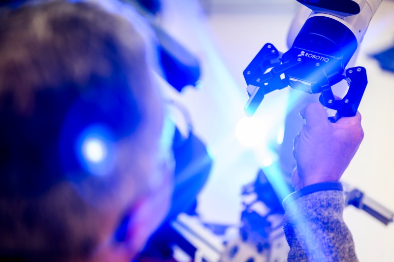 Taskin Padir's hand holding a robotic device in a room with purple and blue lighting.