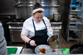 Katie Barry, an executive chef at Northeastern University, plating a dish in a university kitchen.