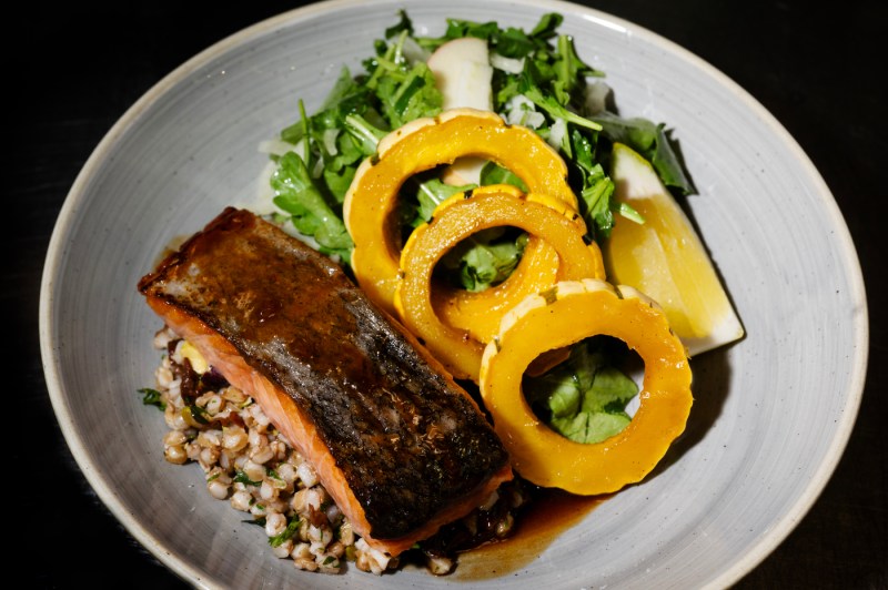 A plated dish featuring pan-seared salmon with crispy skin, fresh arugula salad with sliced pears, and three rings of roasted golden squash arranged on a light gray plate.