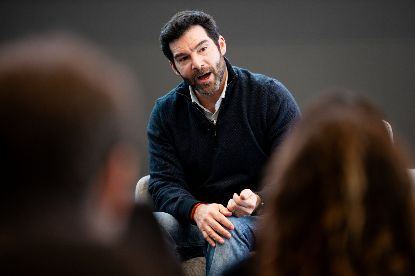 Jeff Weiner speaks animatedly during a fireside chat at Northeastern University. He wears a dark sweater and gestures while addressing the audience, who are visible blurred in the foreground.