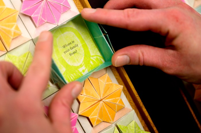 A visitor's hands turn brightly colored pop-up pages of an artist's book reading "Where is your family from?" at Northeastern's Snell Library.