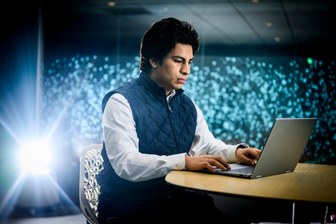 James Elespuru wearing a navy quilted vest over a light blue shirt sitting at a laptop.