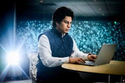 James Elespuru wearing a navy quilted vest over a light blue shirt sitting at a laptop.