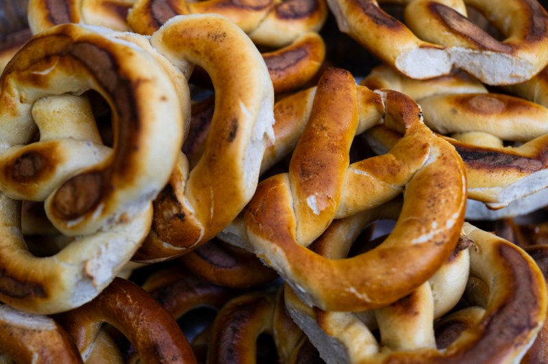 Pile of golden-brown soft pretzels with glossy surfaces and visible salt crystals, showing varied shades from light golden to darker toasted areas.