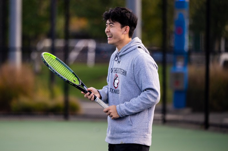 A Northeastern University tennis player smiles while holding a racket during practice at the Carter Field Courts in Boston.