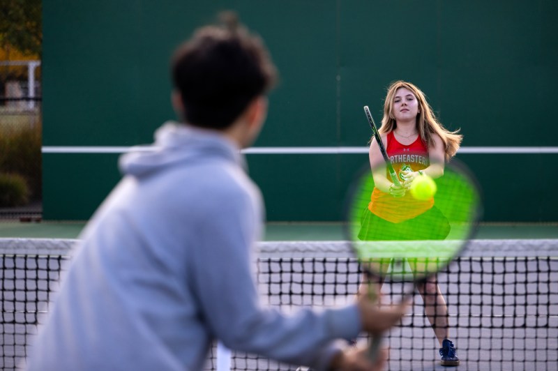 A Northeastern University tennis player prepares to return a shot as an opponent stands at the net during a match at the Carter Field Courts.