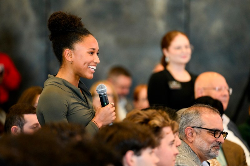 An audience member smiles and looks to the side while seated, with other attendees visible in the background.