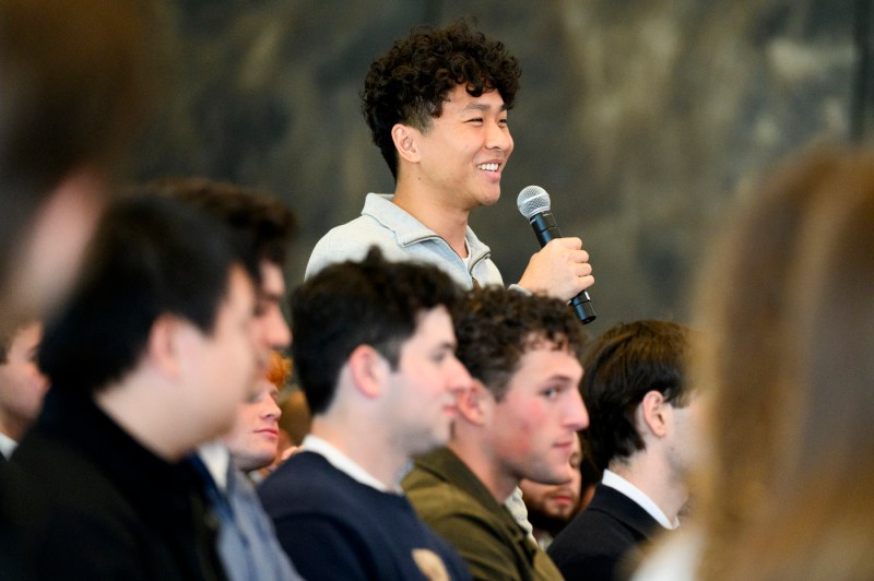 A young person holding a microphone smiles while asking a question from the audience during a panel event.