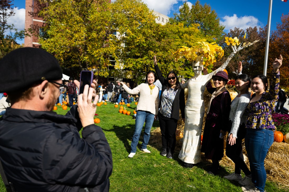 Students pose for a photo with a scarecrow on stilts for Friends and Family Weekend.