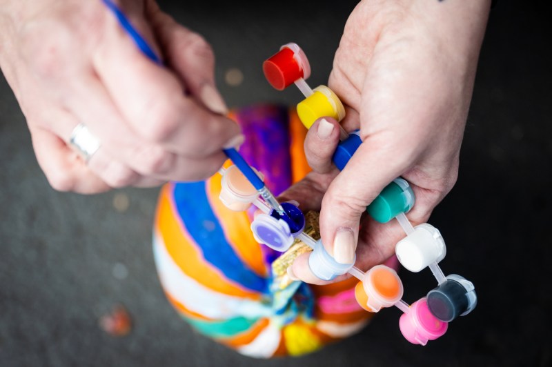 Close-up of a person’s hands painting a small pumpkin in bright colors during Northeastern’s Friends and Family Weekend Fall Festival.