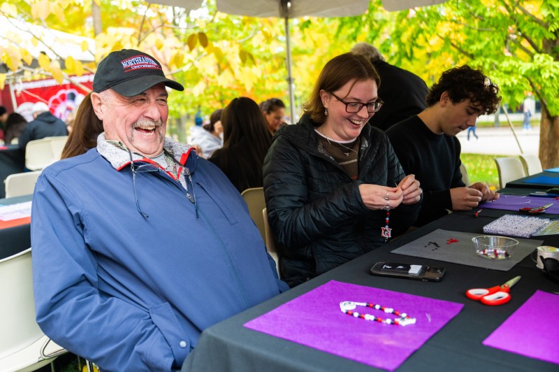 A man and woman smile and laugh as they make bracelets on a table.