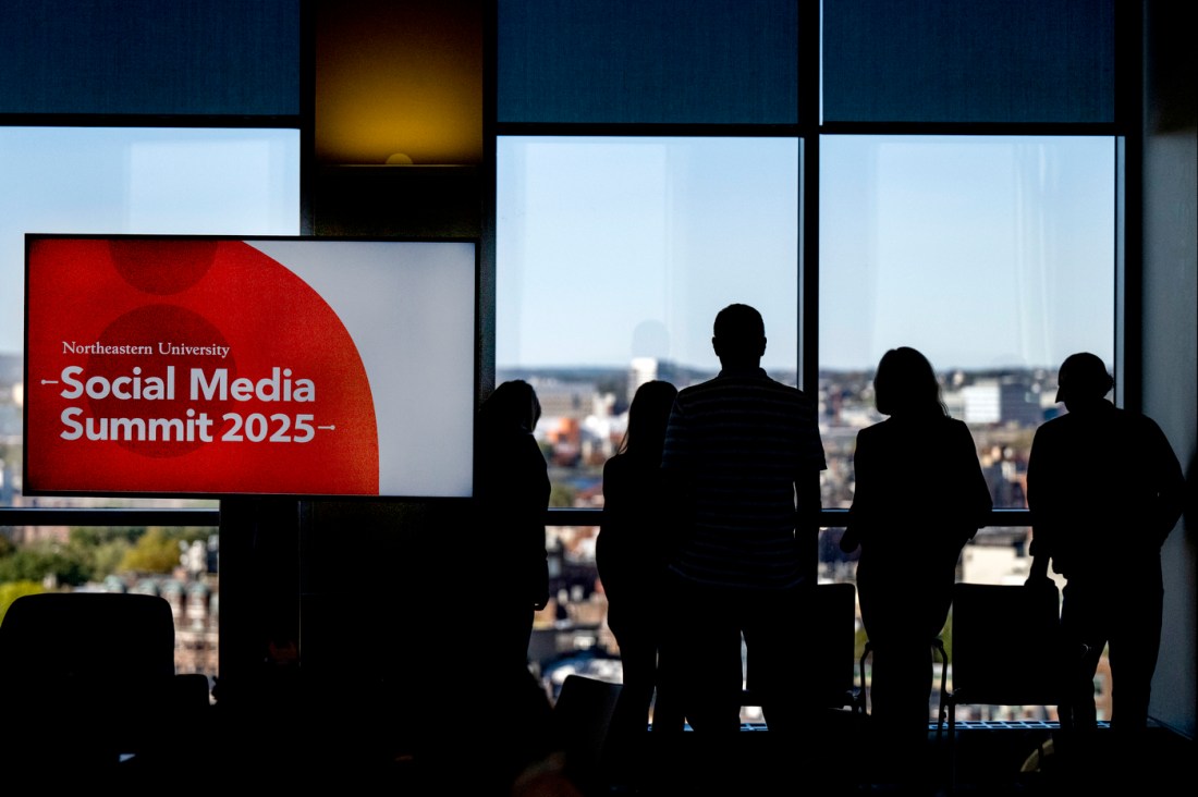 The silhouette of several people standing next to a screen that says 'Northeastern University Social Media Summit 2025' on it. 