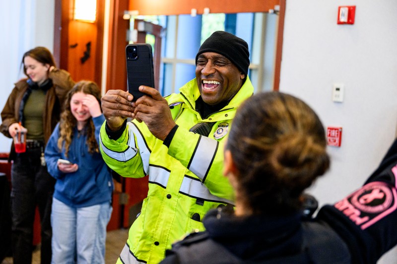 A smiling university police officer holds up a cellphone to take a photograph.