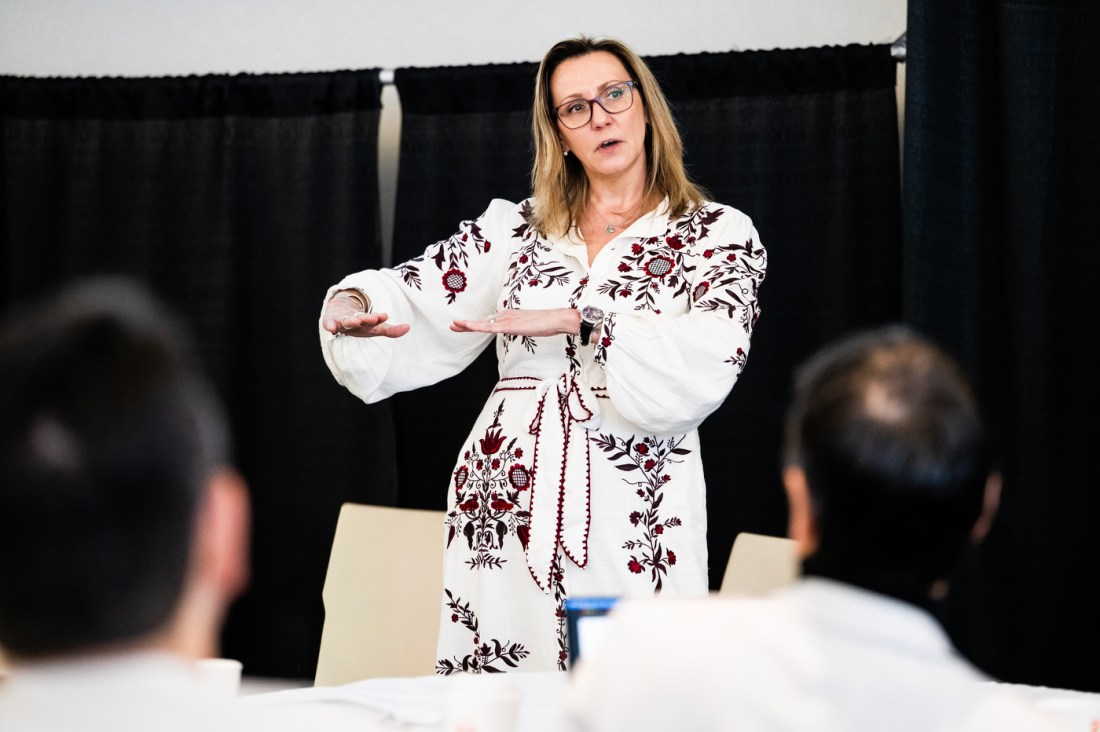 Illena Armstrong, wearing an embroidered white dress, gesturing while speaking at a training event.