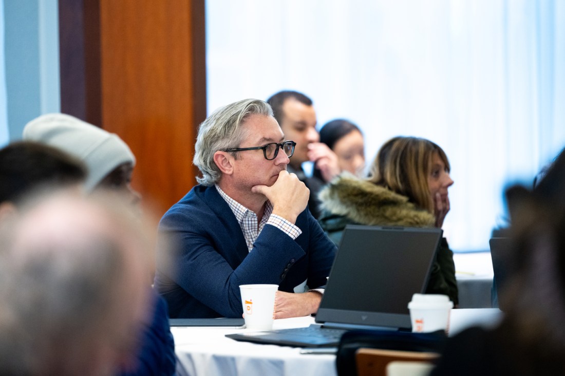 Professionals seated at tables with laptops and notebooks attend a workshop training session.