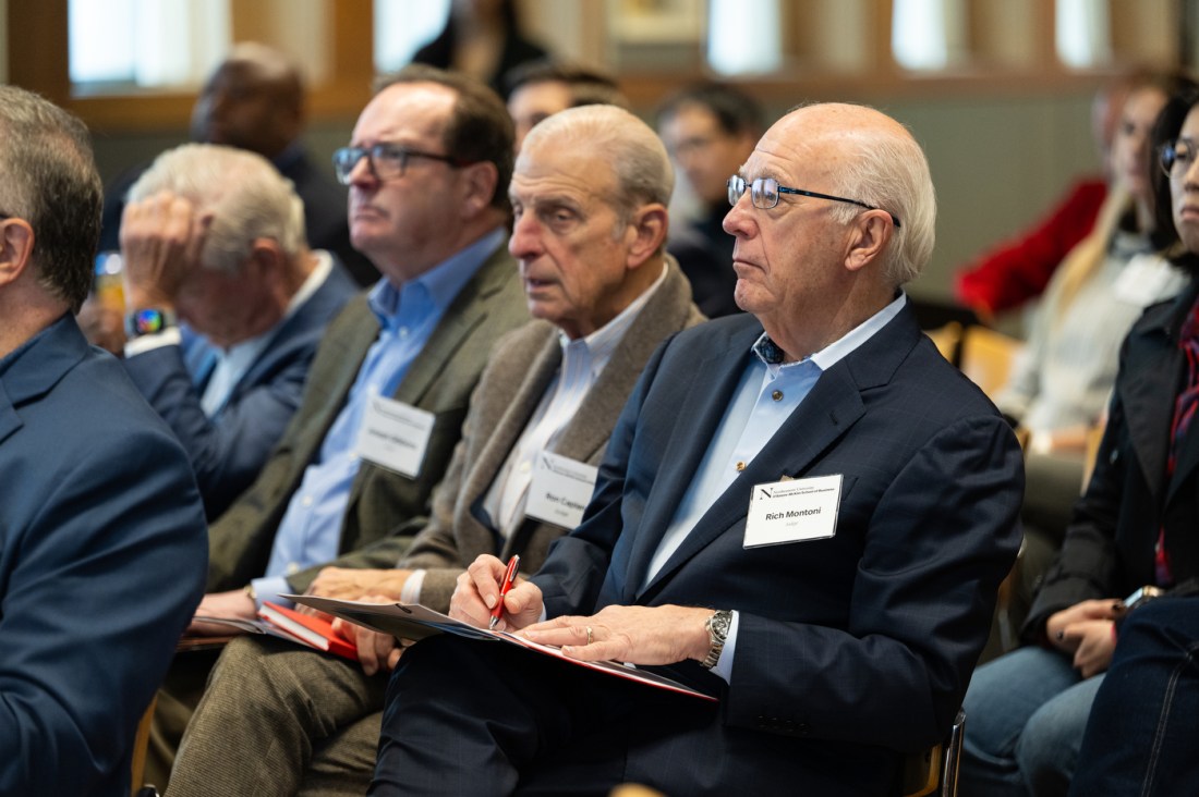 Audience members with white name tags listen attentively during DMSB Day at Northeastern University’s Alumni Center.