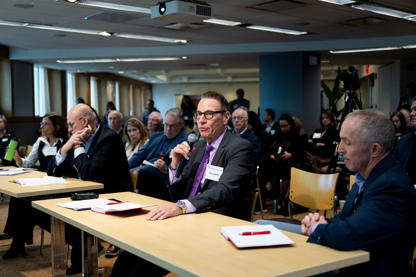 A man with glasses, who is a member of the judging panel, speaks into a microphone from his seat.