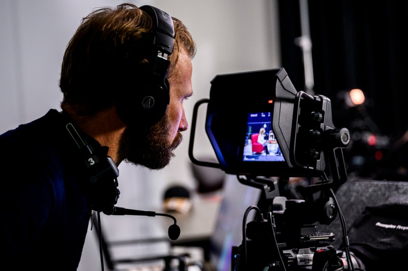 A man is pictured from behind looking at the back of a video camera screen.