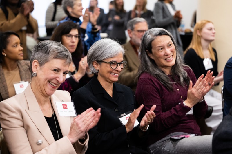 Three woman smile and clap in an audience celebrating the unveiling of a portrait of a Northeastern alumnus.