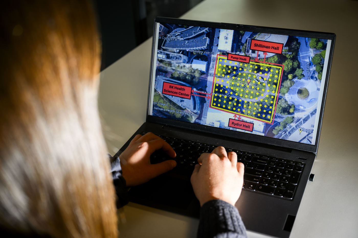 A person with brown hair at work on a laptop, which displays information about a campus project.