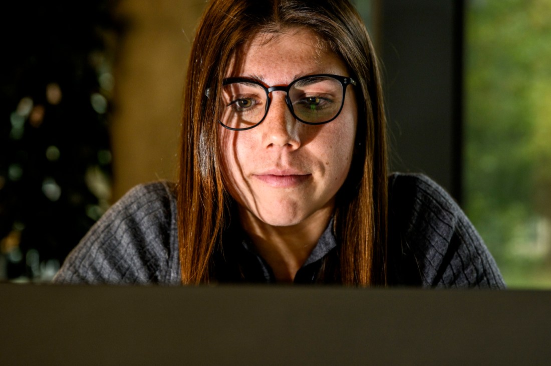 Masters student Emma Ortiz has brown hair and glasses, and is looking down at her laptop.