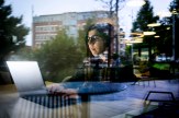 Student Emma Ortiz is typing on a laptop, and is seen through the glass of a building.