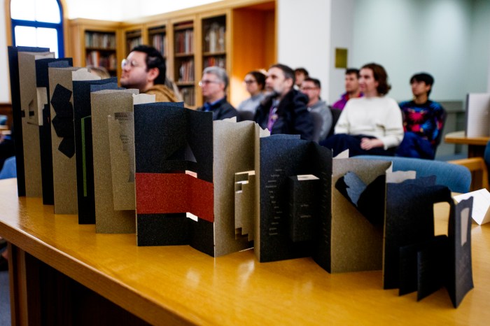 Students examine a row of standing artists' books displayed on a library shelf.