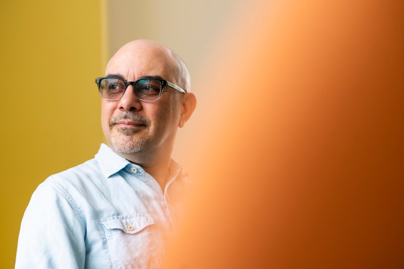 Amílcar Antonio, a bald middle-aged man with glasses, looks over his right shoulder against a yellow backdrop.