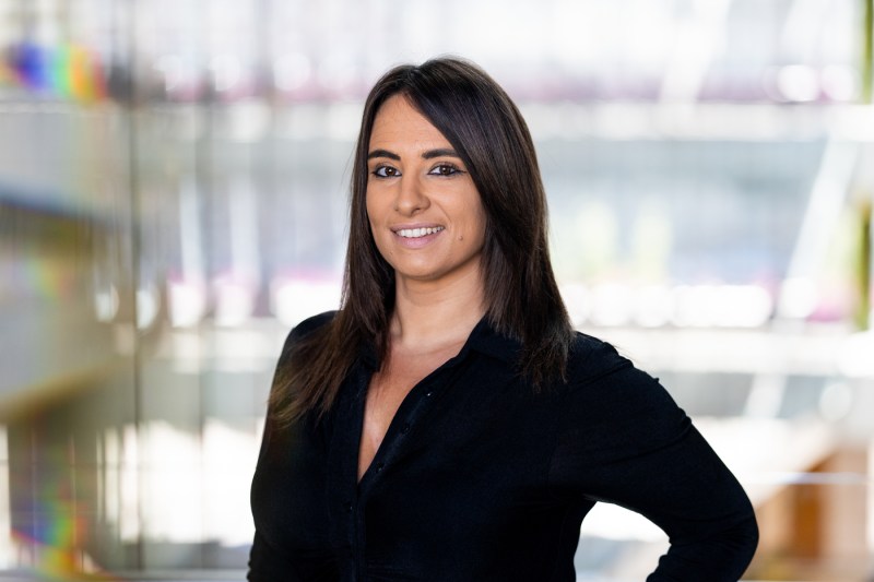 Beatrice Magistro has dark brown hair and a black button-up blouse. She is smiling against a sleek backdrop.