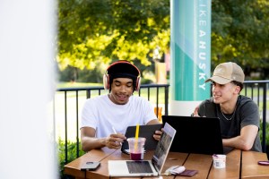 Shem Adams and Daniel Sorokin sit at an outdoor table on Adams Plaza at Northeastern’s Oakland campus, working on laptops and notes.