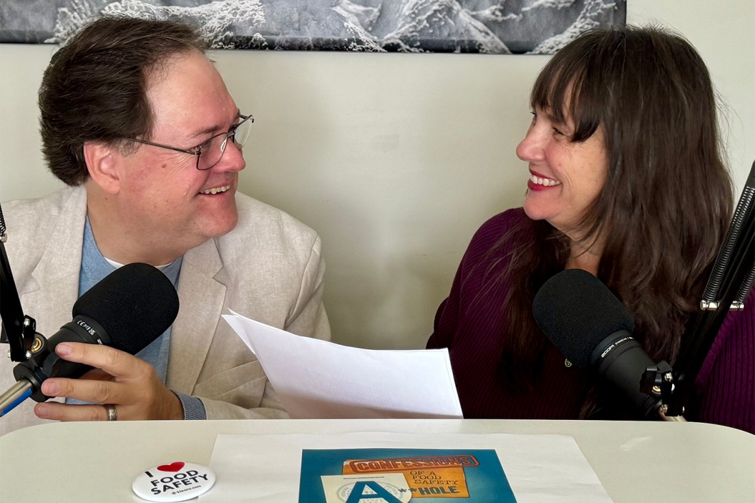 Darin Detwiler and his wife, Gennette Zimmer, smiling at each other in front of microphones with a script between them.