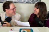 Darin Detwiler and his wife, Gennette Zimmer, smiling at each other in front of microphones with a script between them.
