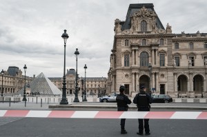Police officers standing in front of the Louvre Museum on a cloudy day.