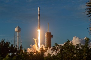 SpaceX Falcon rocket launches from the Kennedy Space Center with flames and smoke billowing as it lifts off the launch pad.