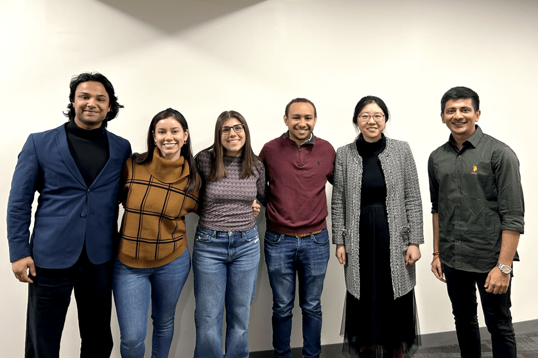 A group of students gather for a photo, standing against a white wall.
