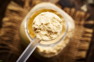 A scoop of whey protein powder held above a jar.