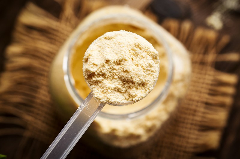 A scoop of whey protein powder held above a jar.