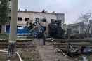 A railway worker stands in front of a destroyed train locomotive under a gray sky.