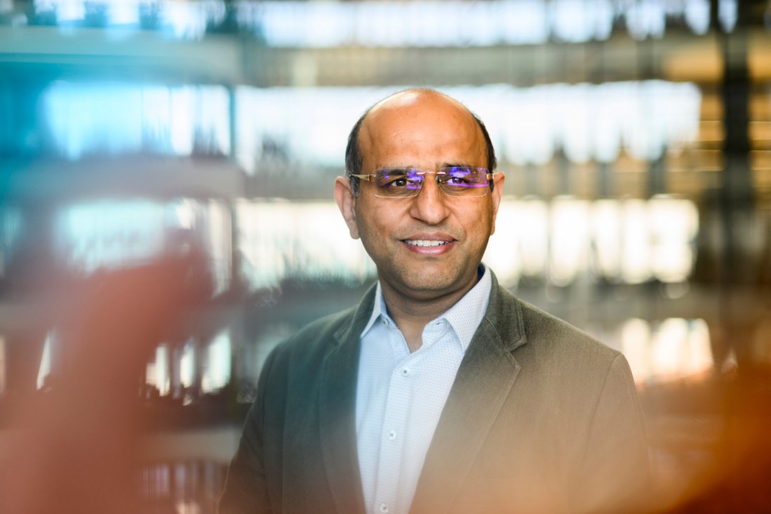 Ravinder Dahiya, a balding middle-aged man with glasses, smiles against a sleek backdrop.