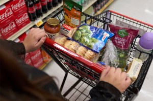 A consumer pushing a grocery cart, with a plethora of different food items displayed.