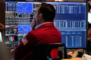 A trader wearing a dark shirt and red vest looking at financial information on his computer.
