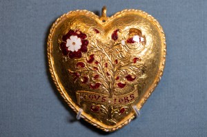 A gold heart-shaped locket with engravings and red jewels on it.