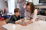 Lee Sowles sitting next to a child at a white countertop in a kitchen. They are both looking at a piece of paper together.