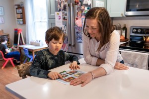 Lee Sowles sitting next to a child at a white countertop in a kitchen. They are both looking at a piece of paper together.