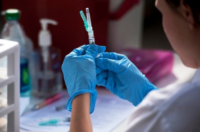 A researcher wearing blue gloves handles several vaccines.