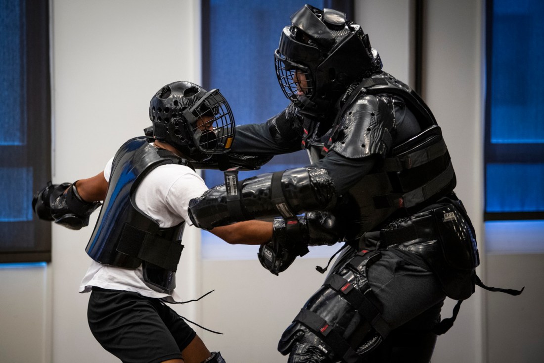 Two Black men with armor and face masks engage in a self-defense drill.