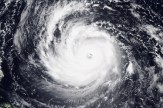 Satellite view of a large hurricane from above, showing a defined circular eye at the center surrounded by dense, spiraling white cloud bands against a dark ocean background.