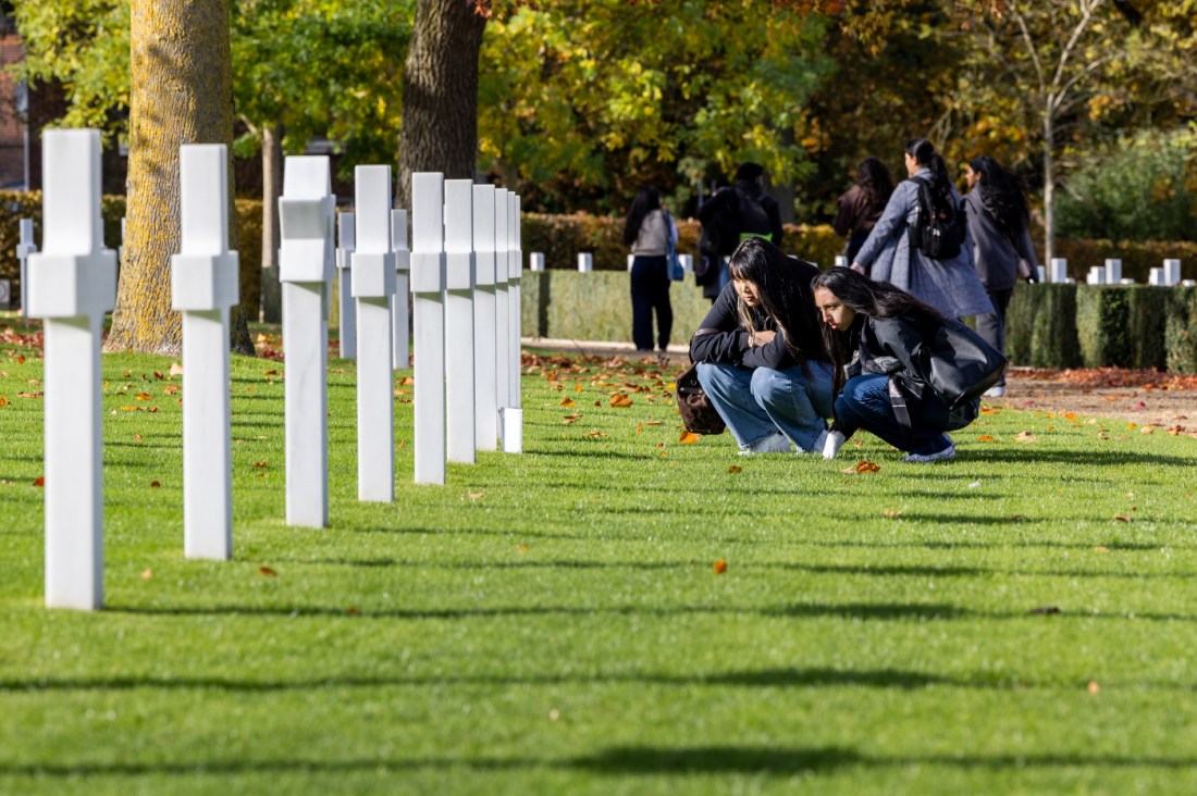 Students crouch in front of white cross markers at the Cambridge American Cemetary.