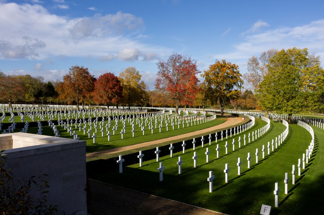 Wide view of the Cambridge American Cemetary with white cross markers in curved rows on green grass. 