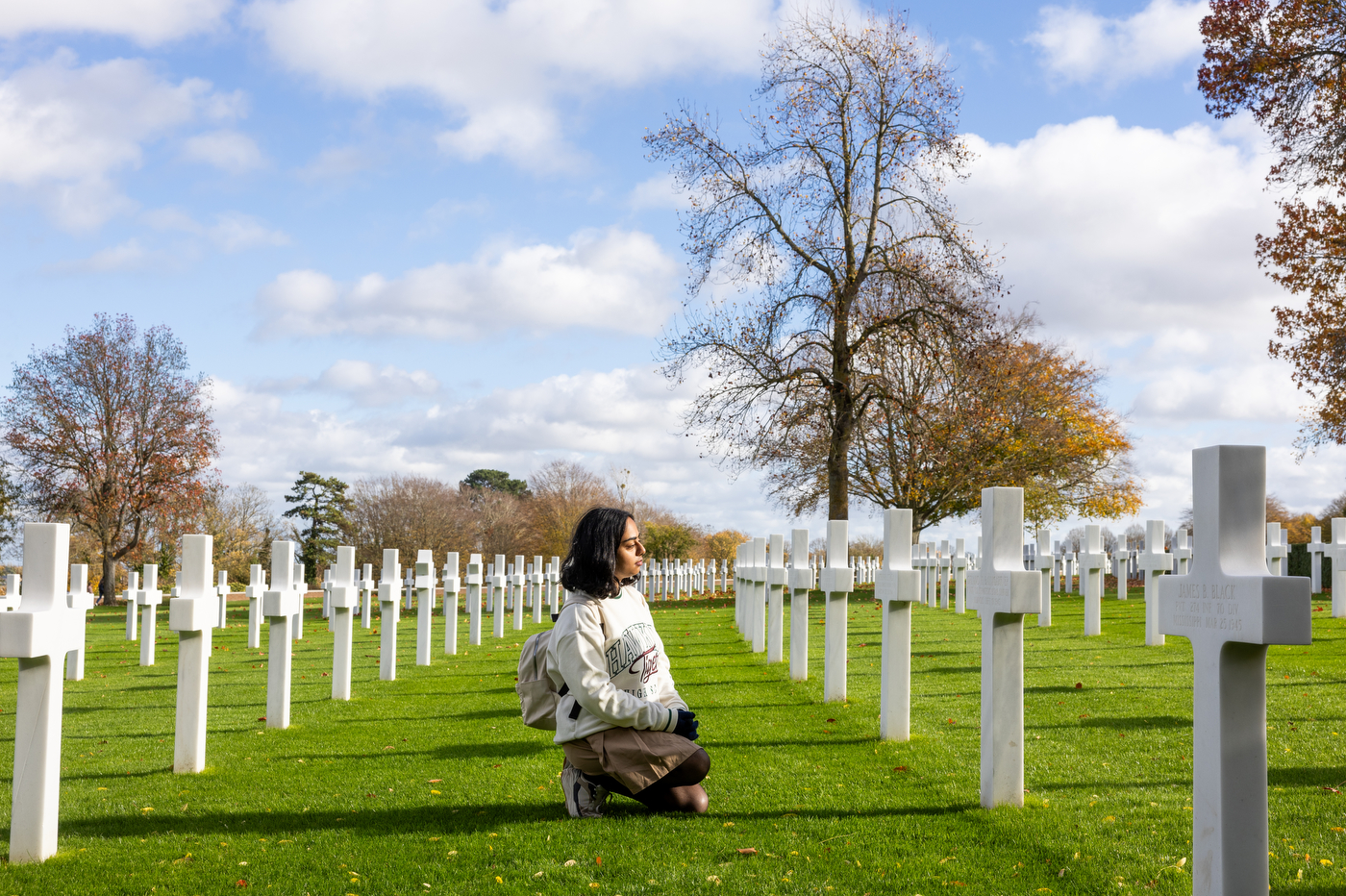 A student looks at rows of white cross markers at the Cambridge American Cemetary.